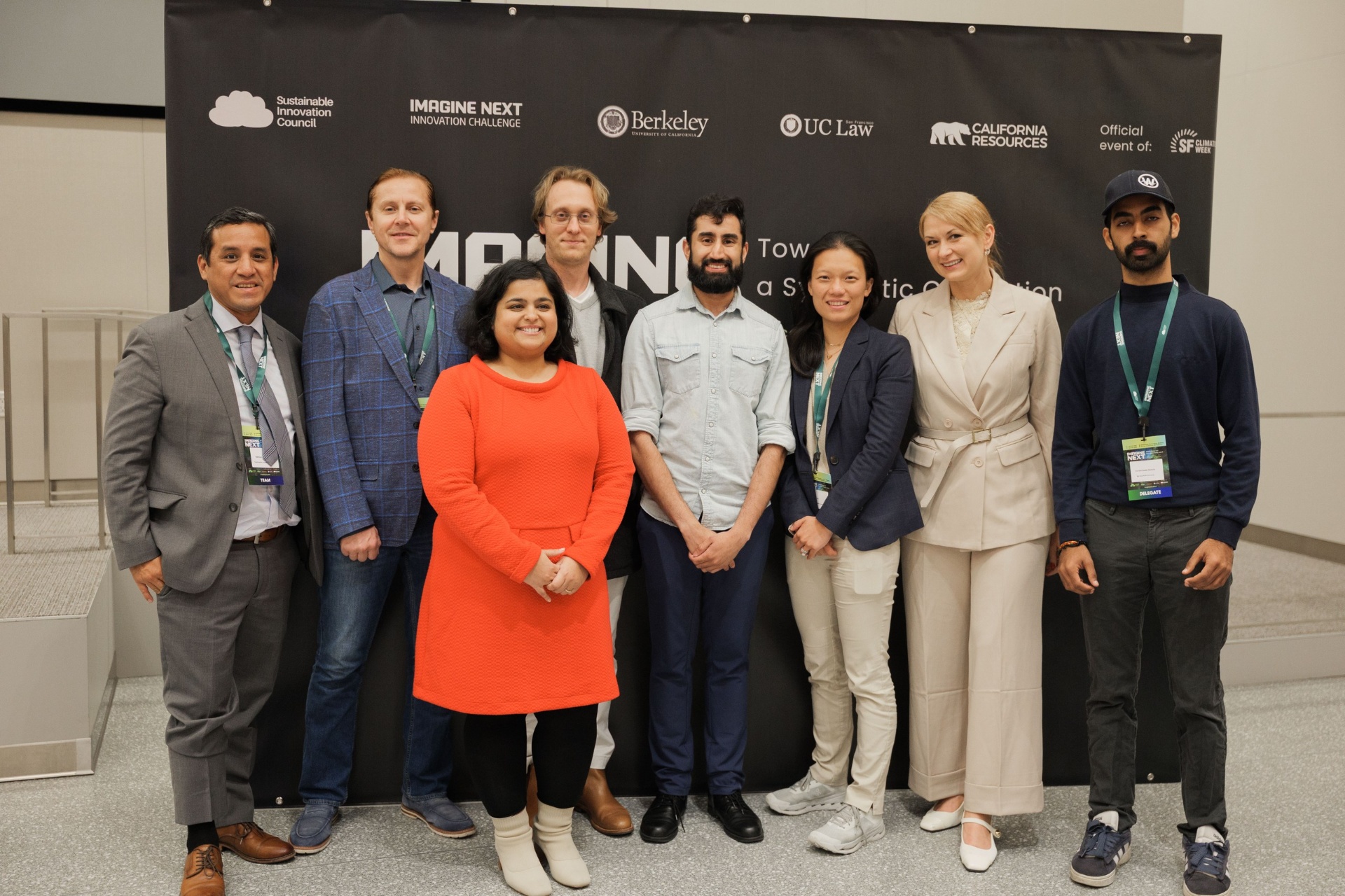 Capital Day Panel 4 'Beyond Priced Rounds' group photo — moderator and panelists with delegate in orange dress posing beneath the Imagine Next Innovation Challenge backdrop at UC Law SF