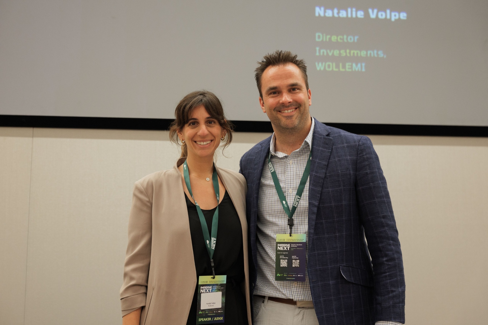 Natalie Volpe of WOLLEMI smiling with a male Imagine Next juror on the Capital Day stage following her fireside chat with Dr. Ryan Gilliam of Fortera
