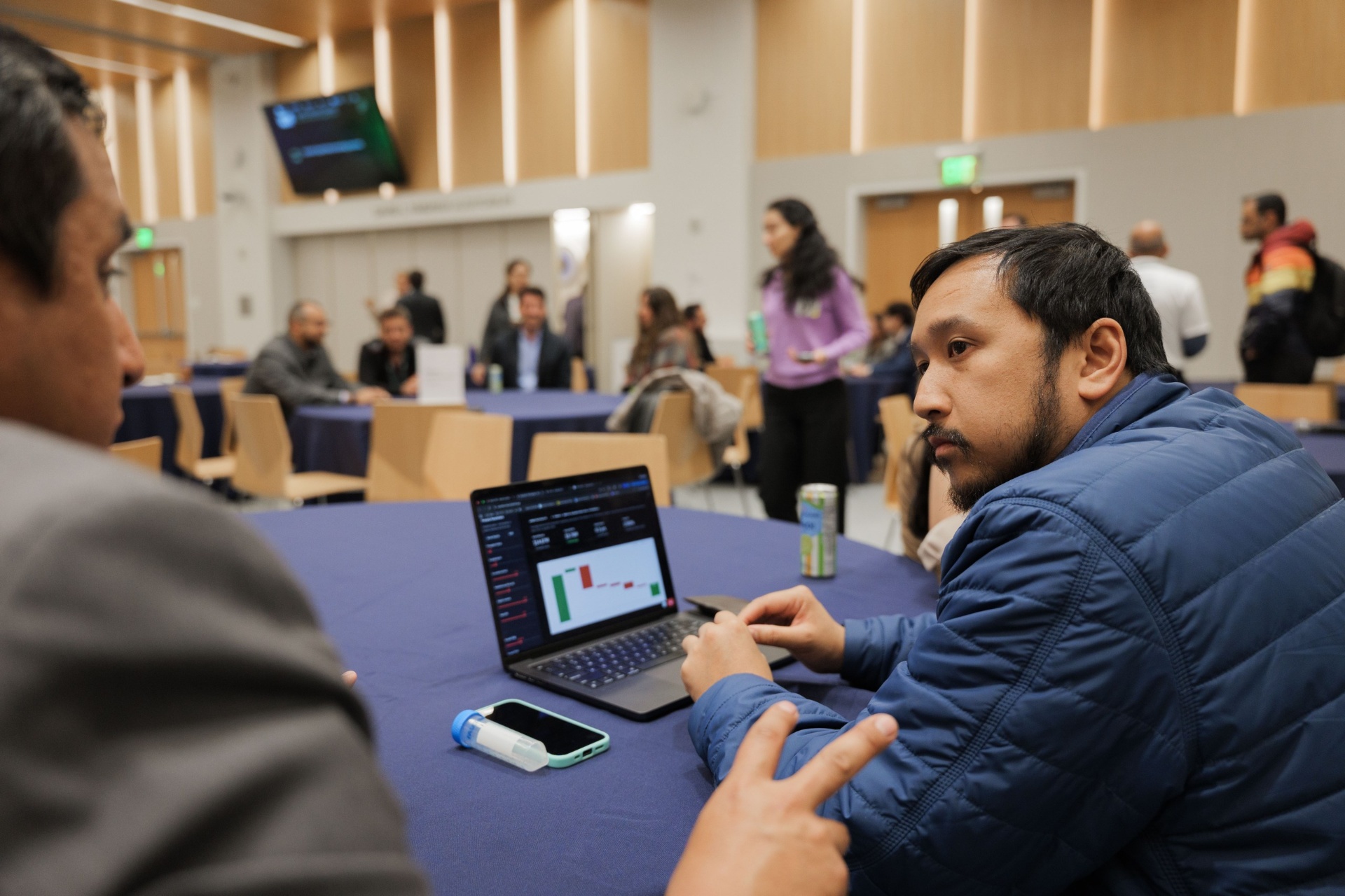 Capital Day Curated Capital Matchmaking Sessions room overview at UC Law SF — delegate in a blue jacket reviewing data on a laptop with the wider matchmaking room visible in the background