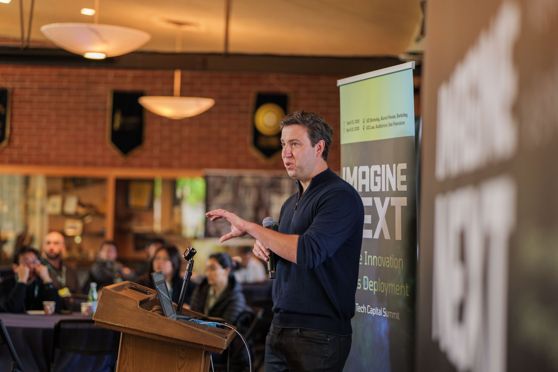 Founder presenting beside the Imagine Next banner at the podium