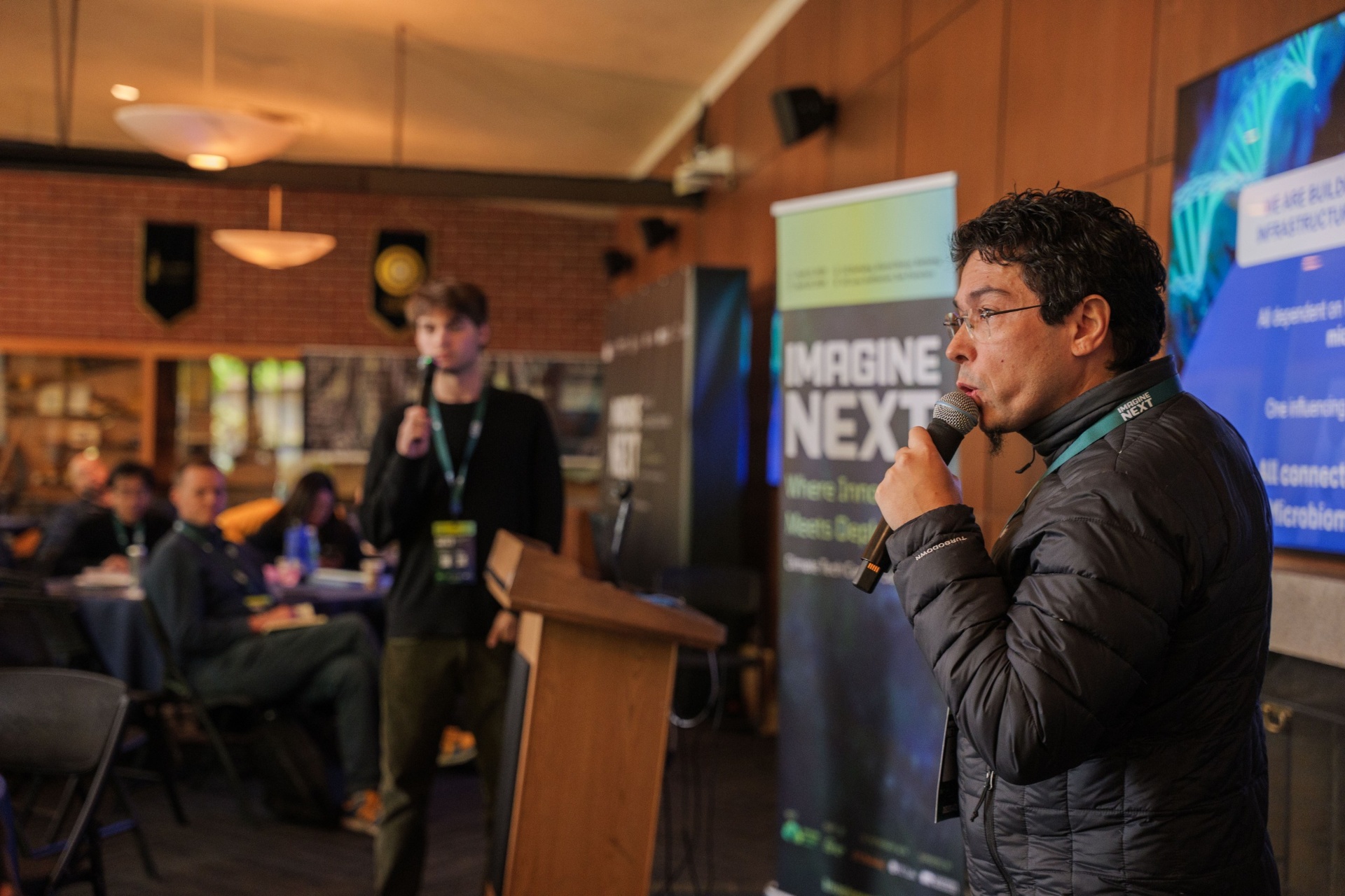 TPM presenter speaking beside the Imagine Next banner