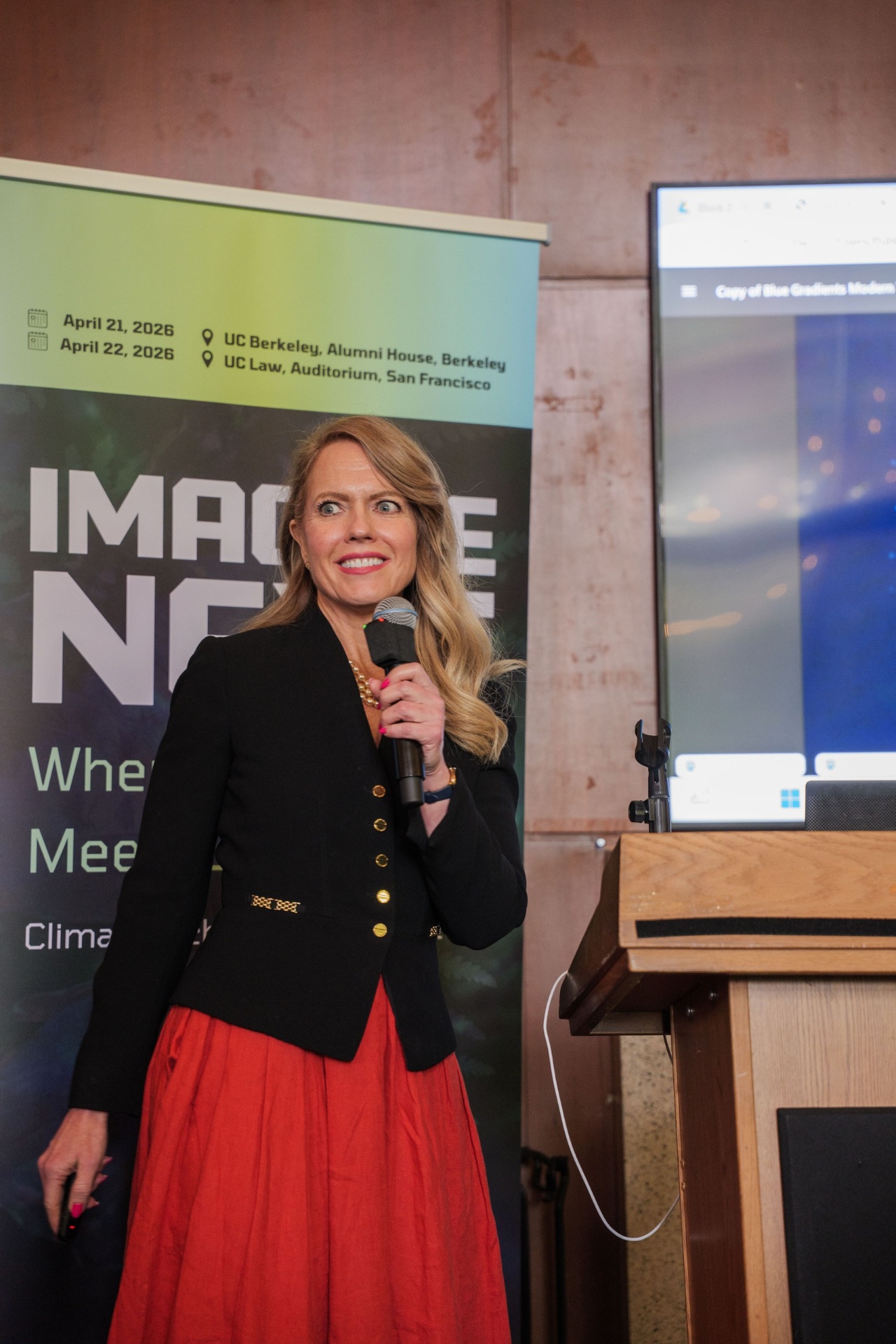 Host smiling beside the Imagine Next banner at the podium